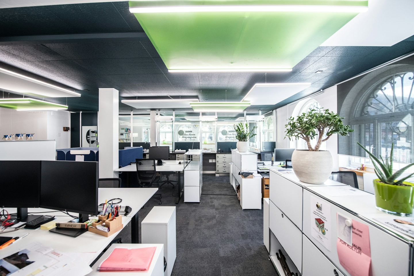 Nowoczesne biuro typu open space z białymi stanowiskami pracy i dużymi oknami.